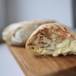 Tasty chicken wrap filled with creamy sauce on a wooden cutting board.