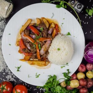 Top view of a savory beef stir-fry with rice, tomatoes, and onions on a ceramic plate.